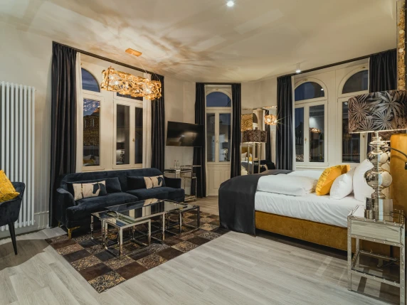 Superior rooms at BS Boutique Hotel Heidelberg. Featuring a golden bed, dark blue sofa, dark curtains, and golden lamp.